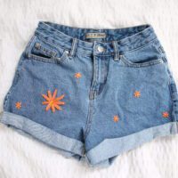 blue denim shorts hand embroidered with a big orange flower and 5 smaller orange flowers