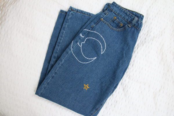 folded up blue jeans showing the hand embroidered white moon with a smily face