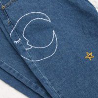 A close up of the hand embroidered moon with a smily face and gold star