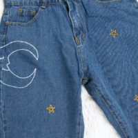 A close up of the hand embroidered moon and gold stars on the legs of the jeans