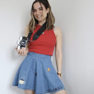 Brunette girl holding a film camera wearing a red crop top and blue denim skirt hand embroidered with Friends TV show inspired motifs