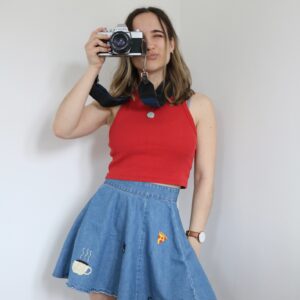 A brunette girl wearing a red top and a blue denim skirt hand embroidered with Friends tv show inspired motifs such as a coffee cup, pizza slice, guitar, and Friends