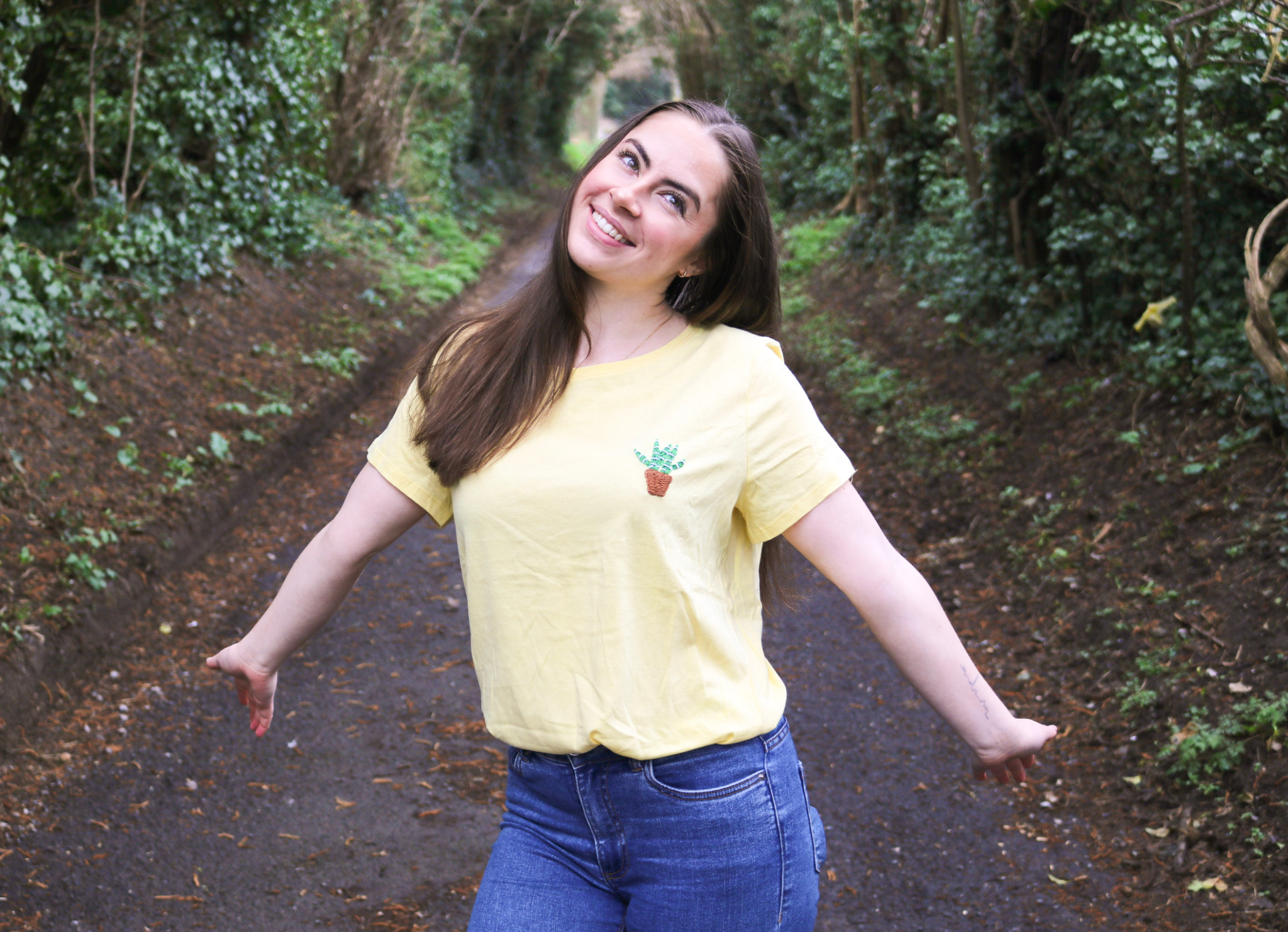 A brunette girl wearing a yellow t-shirt hand embroidered with aloe vera plant