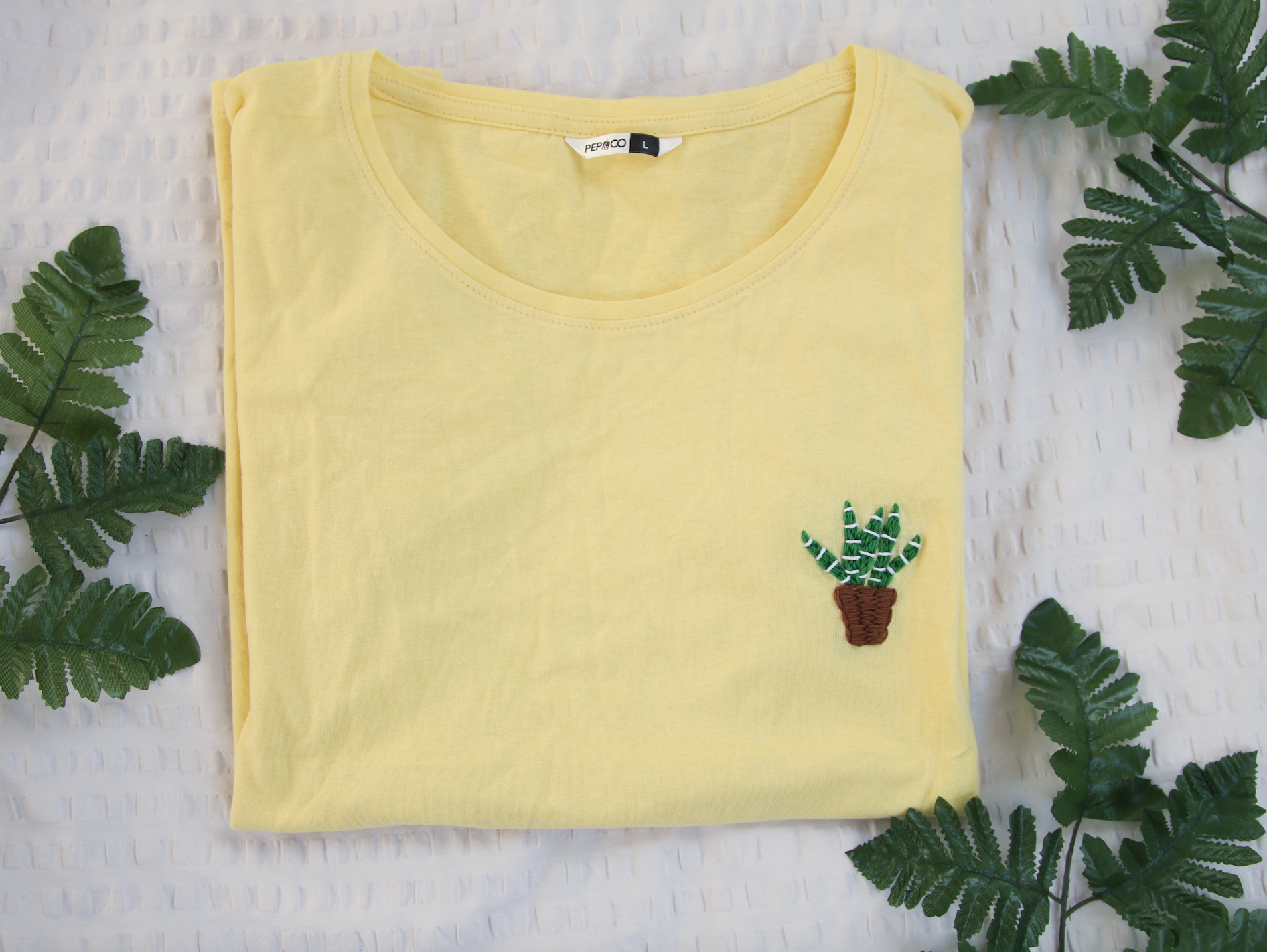A yellow t-shirt hand embroidered with an aloe vera plant
