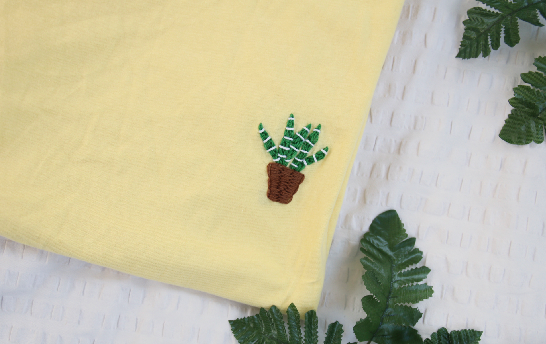 A hand embroidered aloe vera plant on a yellow t-shirt