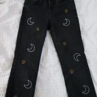 Full view of black jeans hand embroidered with white moons and gold stars up both legs
