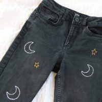 a close up of the embroidery on the black jeans. Embroidered with white moons and gold stars