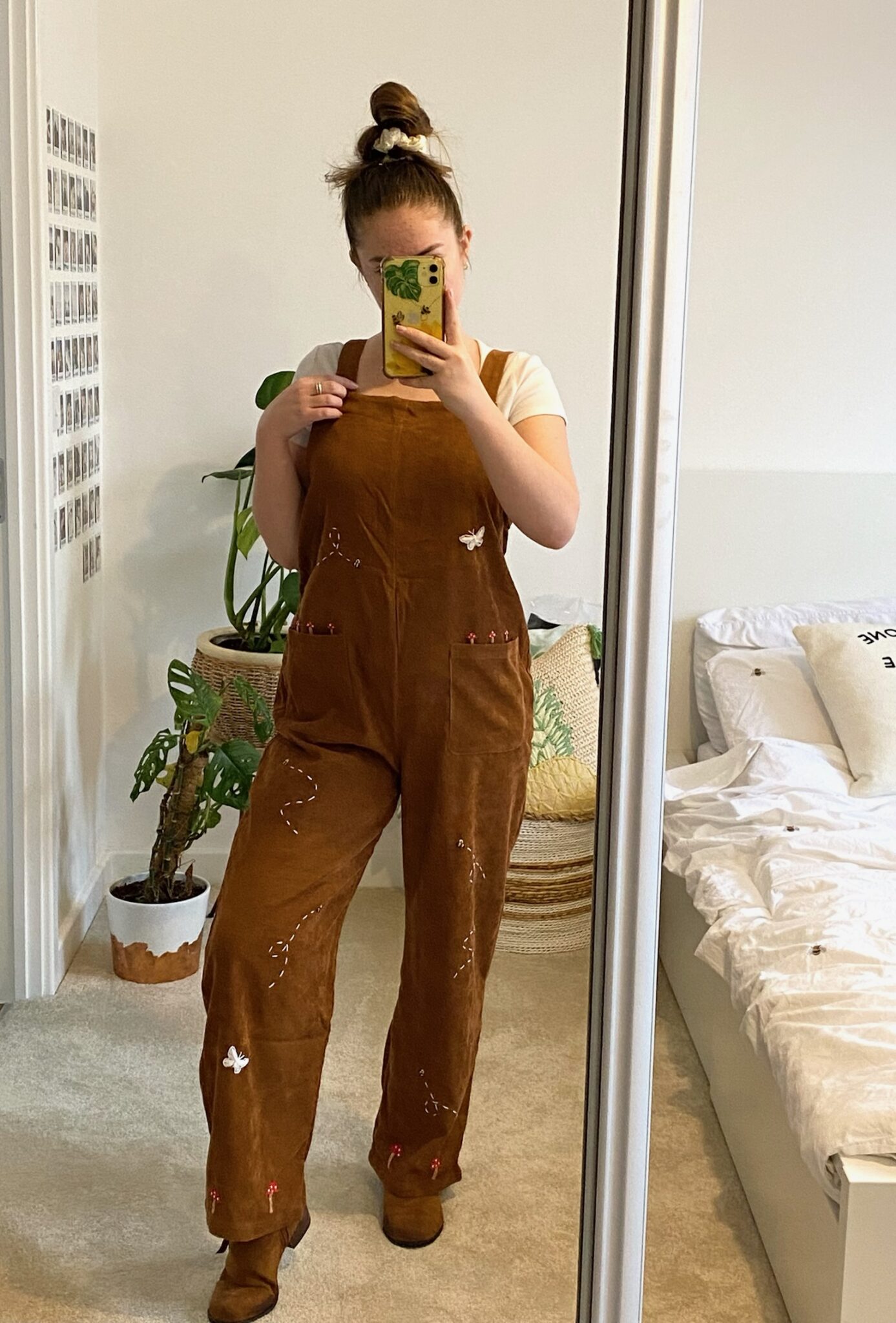 A brunette girl wearing a brown corduroy jumpsuit hand embroidered with butterflies, bees, and mushrooms