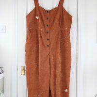 A large brown jumpsuit hand embroidered with butterflies, bees, and mushrooms