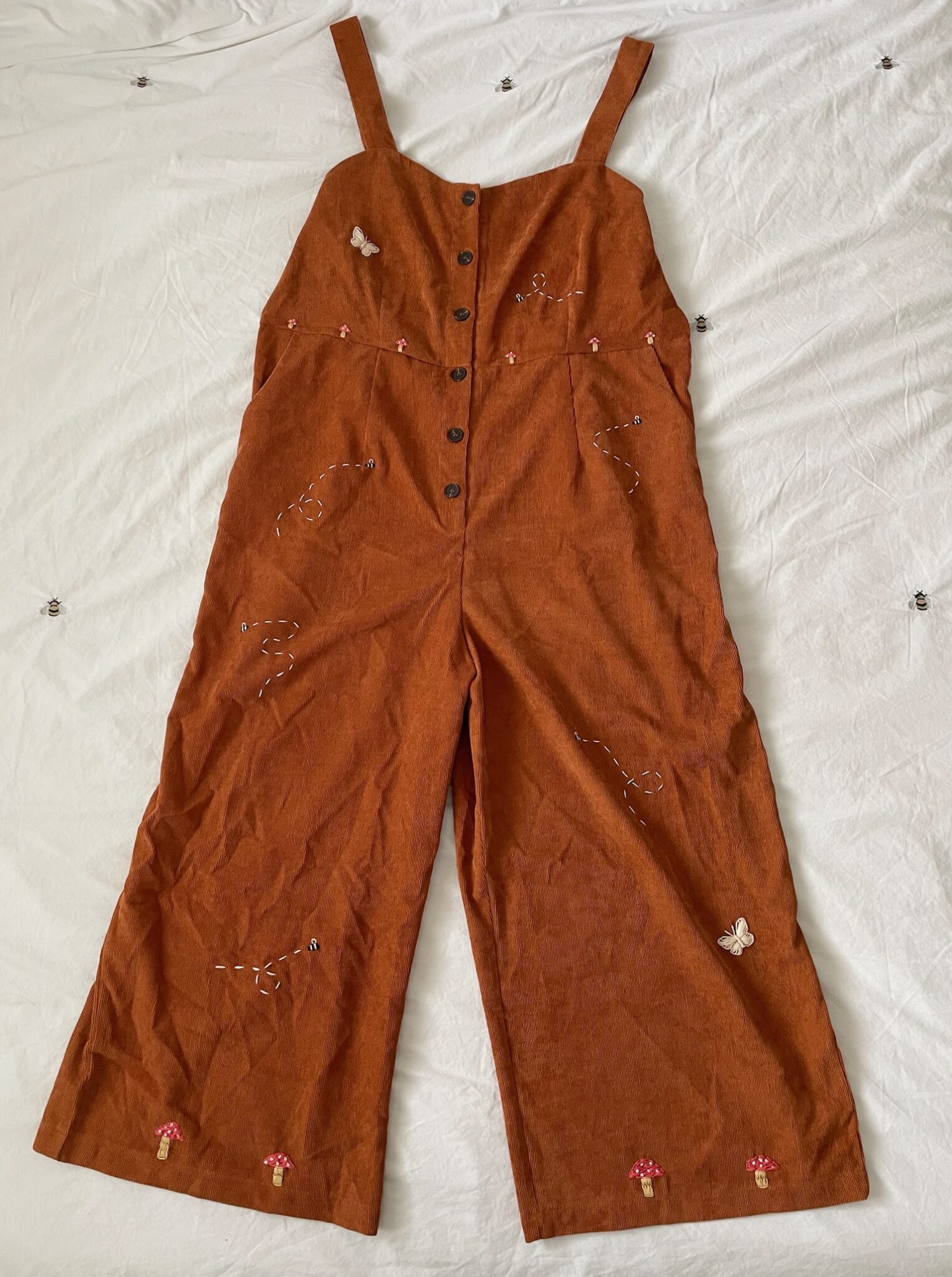 A brown corduroy jumpsuit hand embroidered with mushrooms, bees, and butterflies
