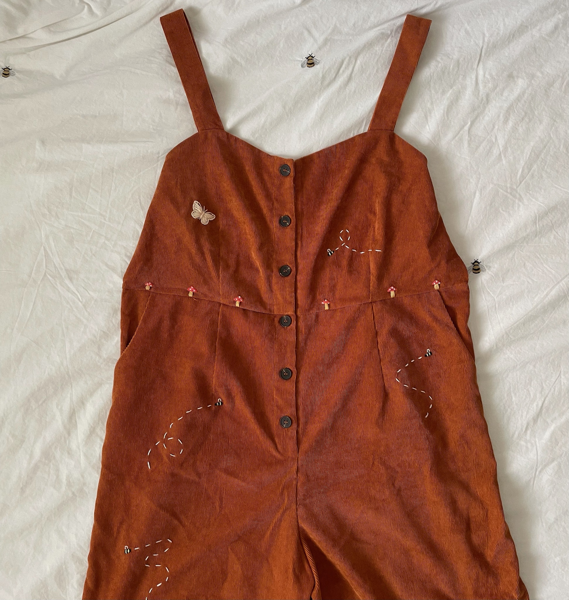 A brown corduroy jumpsuit hand embroidered with mushrooms, bees, and butterflies