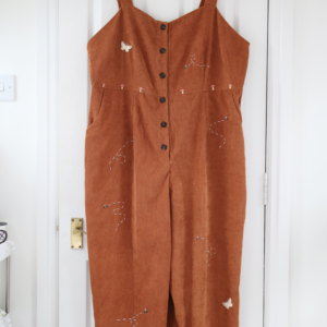 A brown corduroy jumpsuit hand embroidered with mushrooms, bees, and butterflies