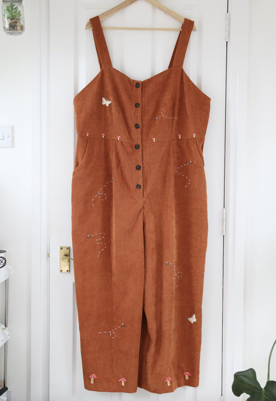 A brown corduroy jumpsuit hand embroidered with mushrooms, bees, and butterflies