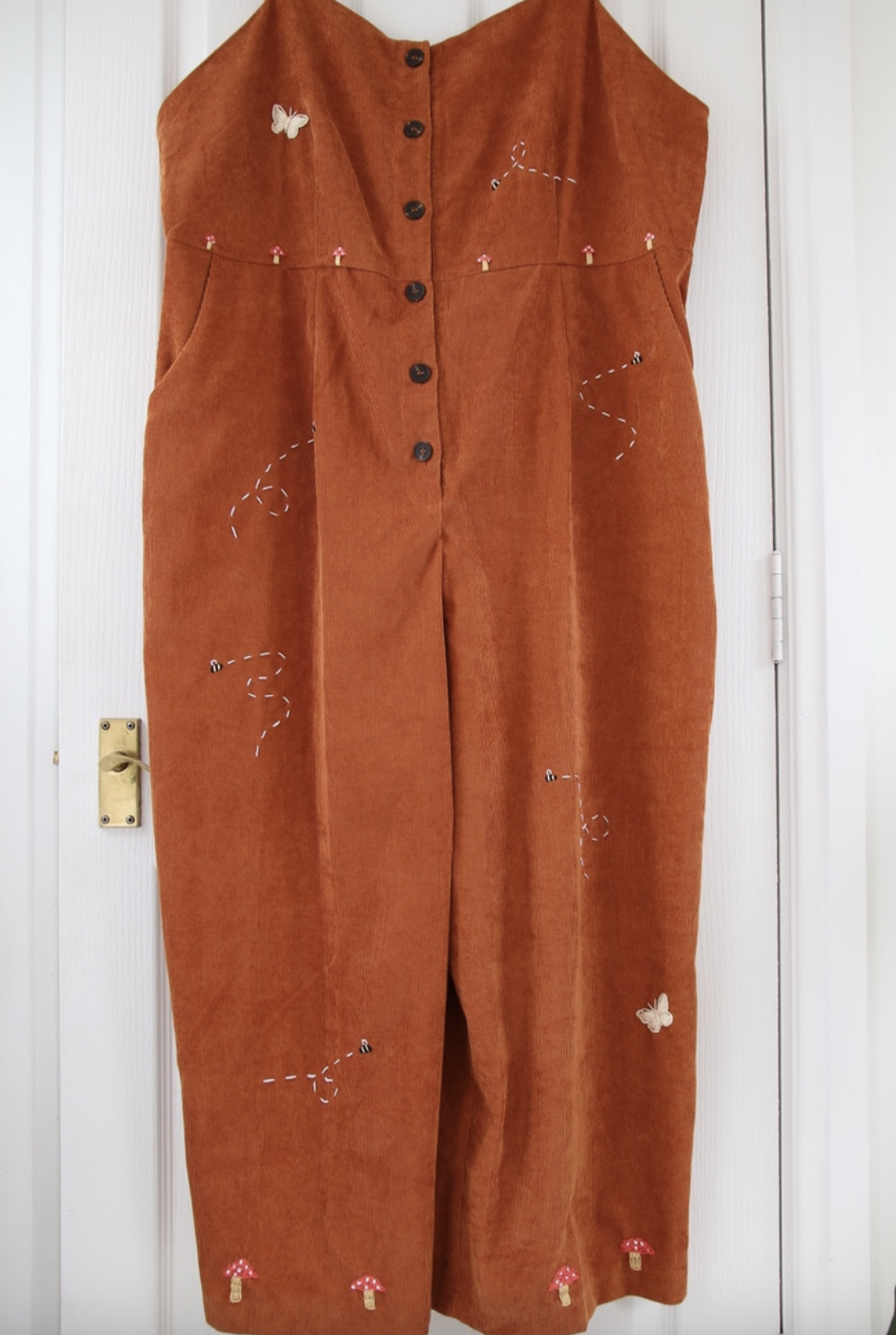 A brown corduroy jumpsuit hand embroidered with mushrooms, bees, and butterflies