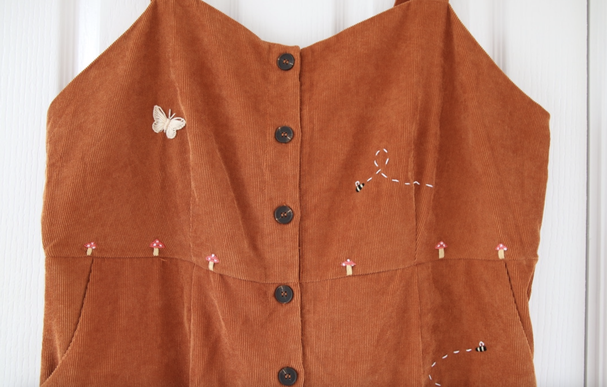 A brown corduroy jumpsuit hand embroidered with mushrooms, bees, and butterflies