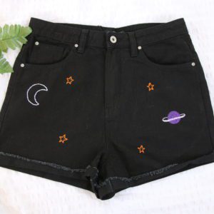 Hand embroidered black denim shorts with a white crescent moon, gold stars and a purple planet