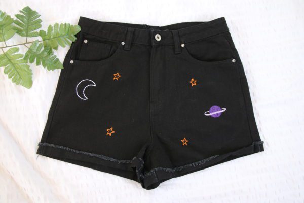 Hand embroidered black denim shorts with a white crescent moon, gold stars and a purple planet
