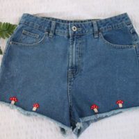 flat lay of blue denim shorts hand embroidered with 4 red mushrooms at the hem