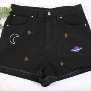 Black denim shorts hand embroidered with a crescent moon, stars, and a purple planet