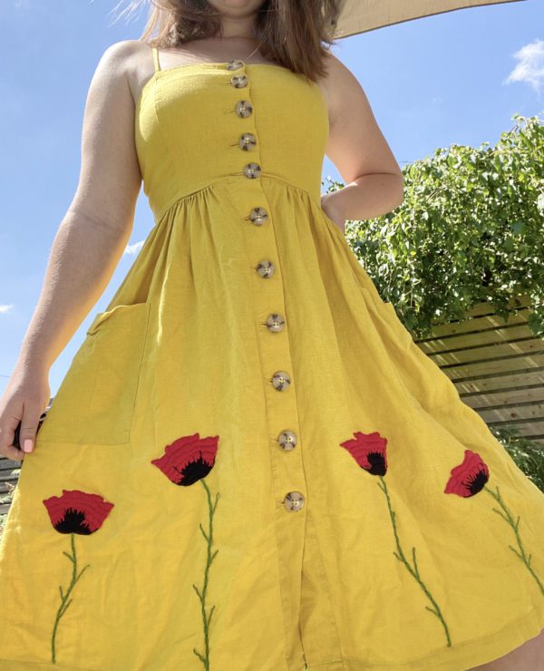 brunette model wearing a yellow dress with hand embroidered red poppies