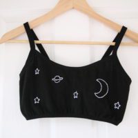 Close up of black bralette hand embroidered with a white moon, stars and planet.
