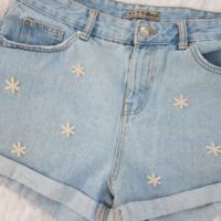 Close up of hand embroidered daisies on blue denim shorts