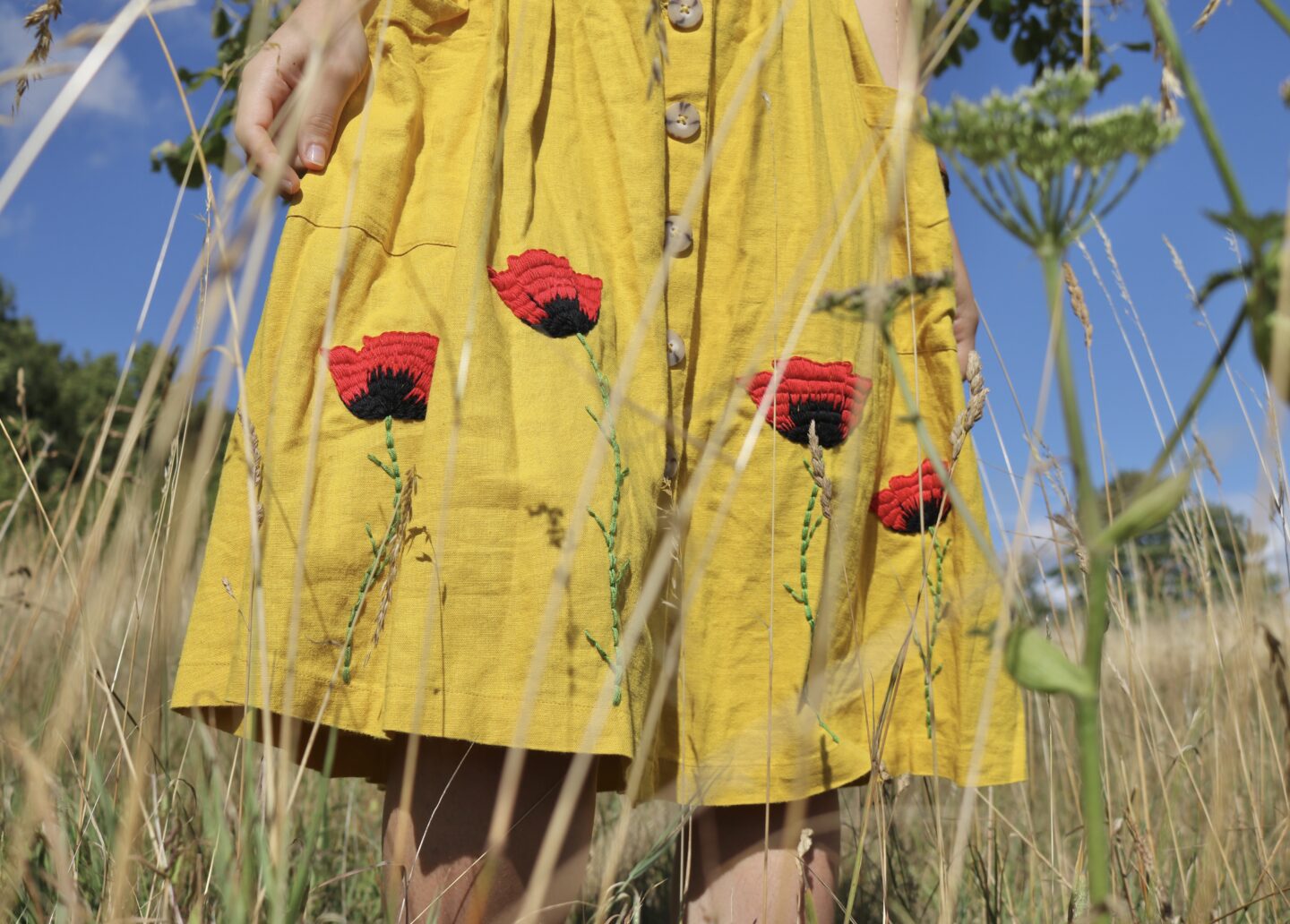 The skirt of a yellow dress hand embroidered with red and black poppies