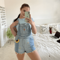 brunette girl wearing blue denim overalls hand embroidered with a sunflowers