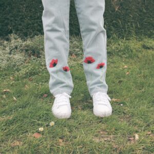 The bottom of a pair of light blue denim straight leg jeans hand embroidered with red poppies growing up the cuff