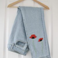folded light blue jeans hand embroidered with big red poppies