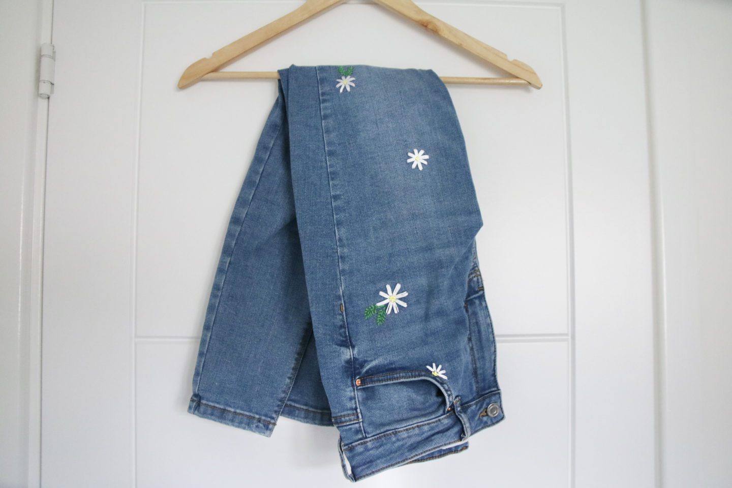 Jeans folded over a hanger. The jeans are blue with white hand embroidered daisies on them