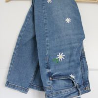 a close up of the hand embroidered daisies on blue skinny jeans