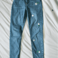 blue skinny jeans laid flat with hand embroidered daisies down one leg