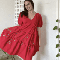 Brunette girl smiling and wearing a red dress hand embroidered with blue flower vines.