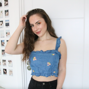 A brunette girl wearing a blue denim crop top with frill sleeves hand embroidered with pink roses