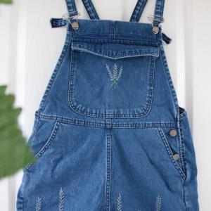 Blue denim overall shorts hand embroidered with lavender growing up the hem