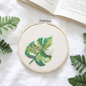 A 6 inch embroidery hoop and embroidered Monstera leaf in varying shades of green.