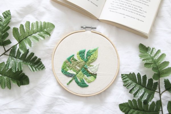 A 6 inch embroidery hoop and embroidered Monstera leaf in varying shades of green.