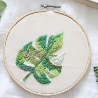 Close up of a hand embroidered monstera leaf in varying shades of green
