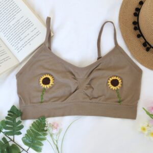 A flatlay of a brown bralette hand embroidered with sunflowers surrounded by a book, leaves, and a hat