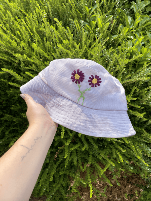 hand holding purple bucket hat hand embroidered with purple cosmos flowers