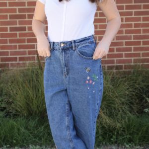 Close up of hand embroidered pink flowers and a bee on blue mom jeans