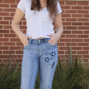 half shot of a brunette girl wearing blue skinny jeans hand embroidered with dark blue flowers