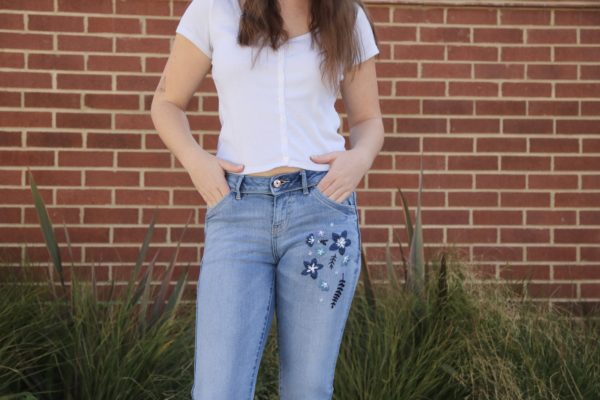 half shot of a brunette girl wearing blue skinny jeans hand embroidered with dark blue flowers