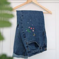 Blue mom jeans folded up showing the hand embroidered pink flowers, green leaves and a bee