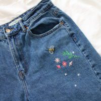 close up of the top of the jeans showing the embroidered flowers, greenery and a bee