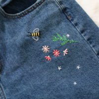 close up of hand embroidered bee, pink flowers and greenery by the front pocket