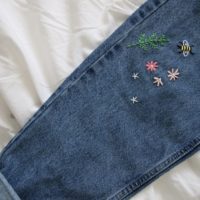 close up of hand embroidered pink flowers, greenery and a bee on the leg