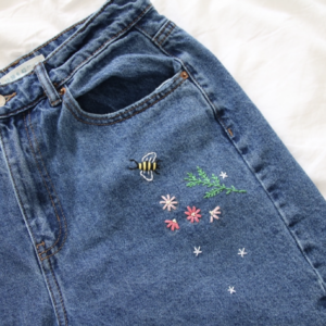 The wait of blue denim mom jeans hand embroidered with pink flowers, leaves, and a bee