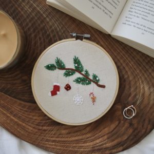 A hand embroidered 6 inch hoop with a snowy branch and hanging ornaments